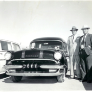 Two men in suits and hats standing next to a car, circa 1955
