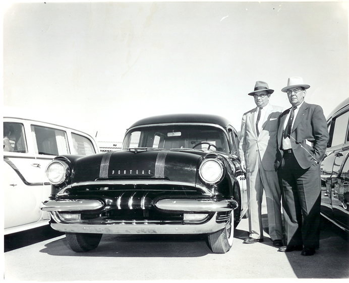 Two men in suits and hats standing next to a car, circa 1955
